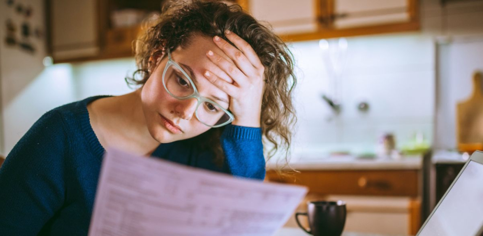 una mujer sosteniendo su cabeza mirando un pedazo de papel